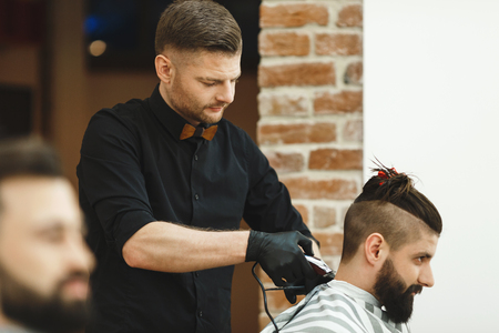 Dark haired man wearing black shirt doing a haircut for man with long black hair at barber shop, copy space.の写真素材