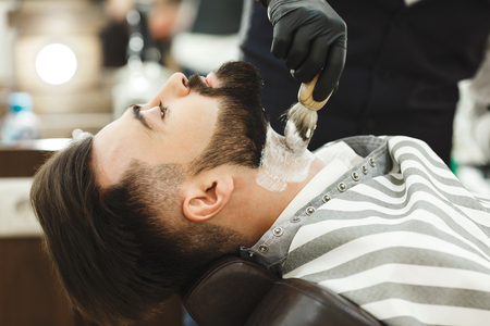 Hands in black gloves making a beard form for man with black hair and beard at barber shop, close up, portrait.の写真素材