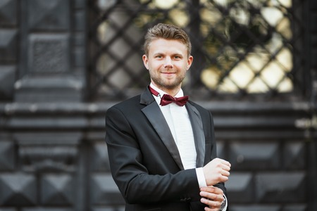Wedding photo shooting. Bridegroom standing outdoor. Man wearing white shirt, black jacket and...
