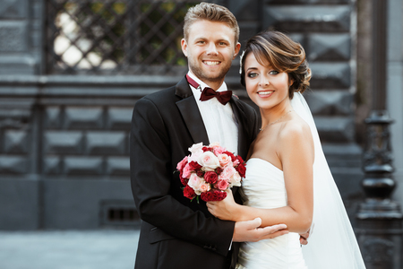 Wedding photo shooting. Bride and bridegroom smiling and embracing. Holding bouquet. Outdoor, waist upの写真素材
