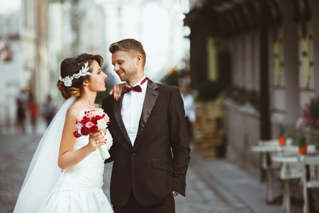 Wedding photo shooting. Bride and bridegroom at street Looking at each other, holding bouquet. Outdoorの写真素材