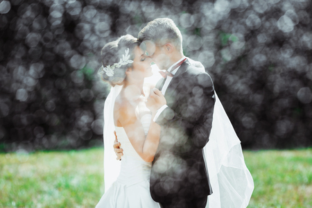 Wedding photo shooting. Bride and groom under heavy rain, holding hands of each other. Very close to each other. Closed eyes. Outdoorの写真素材