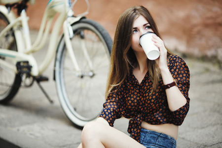 Pretty girl is drinking coffee on tiled pavement in old cityの写真素材