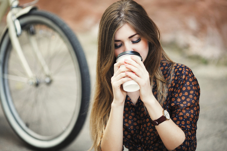 Beautiful girl is drinking coffee on tiled pavement in old cityの写真素材
