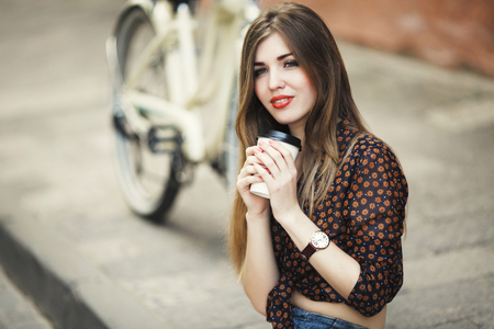 Pretty girl wearing on blouse is drinking coffee on tiled pavement in old cityの写真素材