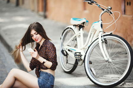 Gorgeous girl with long hair wearing on blouse and shorts is sitting on pavement in old cityの写真素材