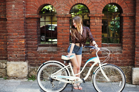 Happy girl with bicycle standing near the brick buildingの写真素材