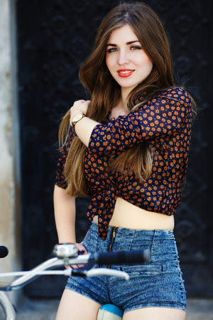 Lively young woman with long hair is sitting on the bicycle and looking at the camera on the streetの写真素材