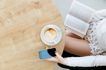 Girls legs, cup of coffee, book and mobile phoneの写真素材