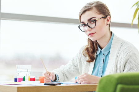 Girl with glasses sitting with colorful paintsの写真素材