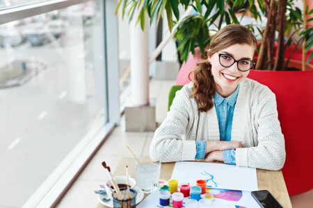 Girl with glasses sitting with colorful paintsの写真素材