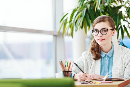 Girl with glasses sitting with colorful pencilsの写真素材