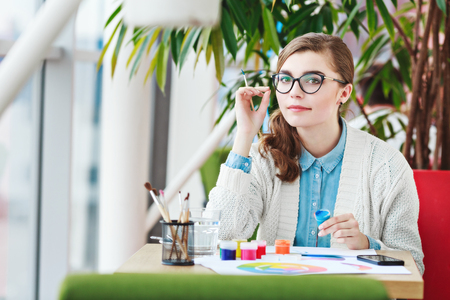 Girl with glasses sitting with colorful paintsの写真素材