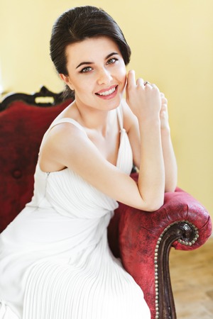 Woman in white bridal dress kneeling on red armchairの写真素材