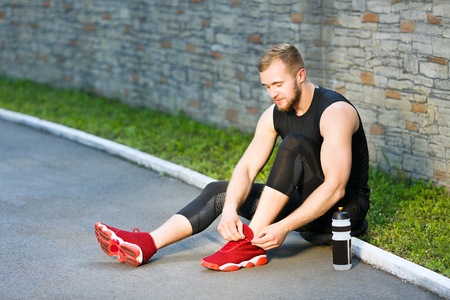 Sportsman sitting with water and tightening lacingsの写真素材