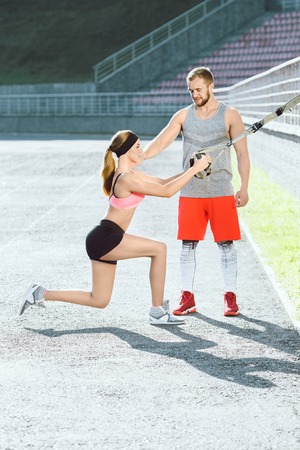 Sporty girl doing exercises with training loop and coachの写真素材