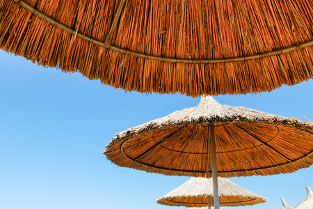 Three beach umbrellas made of straw at blue sky backgroundの写真素材