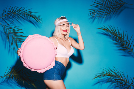 Young girl posing with huge macaroon. Beautiful blonde girl. Blue. Summer. Candy lover. Hot body. Palms. model posing. Big sweets. Funny girl. Sexy body. Portrait. Fit girl. Enormous macaroon. Perfect smile.の写真素材