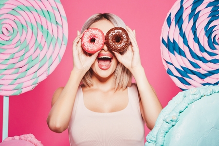 Beautiful girl posing with sweets at pink backgroundの写真素材