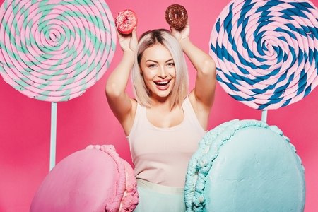 Beautiful girl posing with sweets at pink backgroundの写真素材