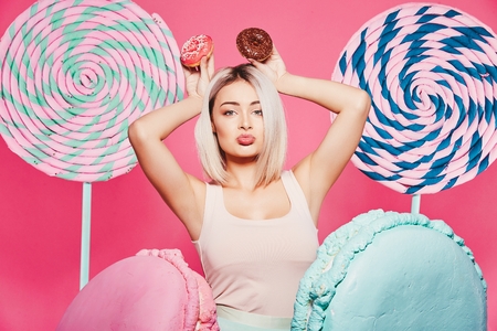 Beautiful girl posing with sweets at pink backgroundの写真素材