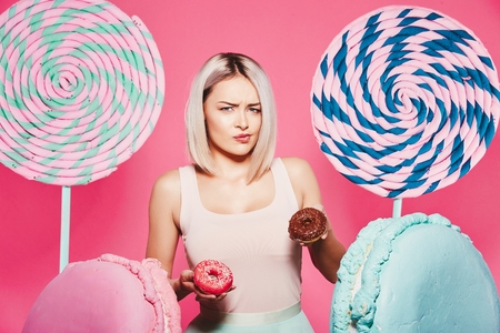 Beautiful girl posing with sweets at pink backgroundの写真素材