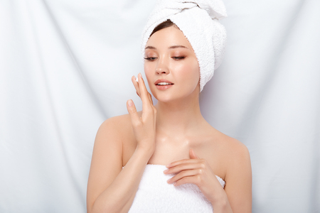 girl with perfect skin in bath towel applying facial cream and looking down, preety female after spa putting on moisturizerの写真素材