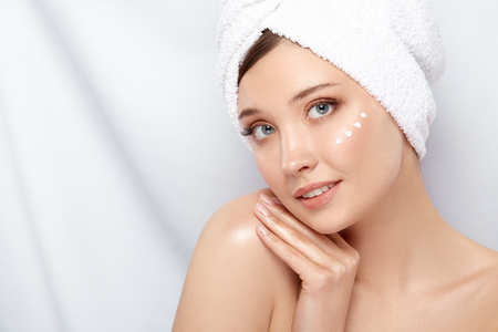 attractive girl with towel on her head touching her shoulder and having cream under her face, copy space, close-upの写真素材