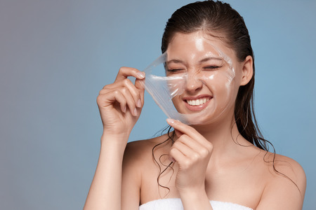 happy woman removing with hardness her facial mask and smiling, pretty young girl doing spa procedures, copy spaceの写真素材