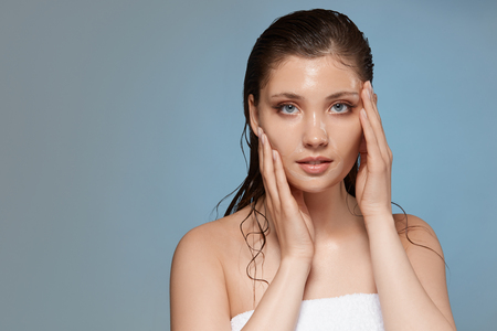 attractive girl in bath towel looking to te camera and touching her face, copy space, after showwr woman with wet hairの写真素材