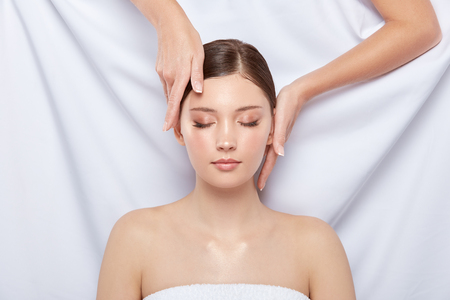 arms touching womans face on white background, massage theraphy for head and face, person lying down in spa, women treatmentの写真素材