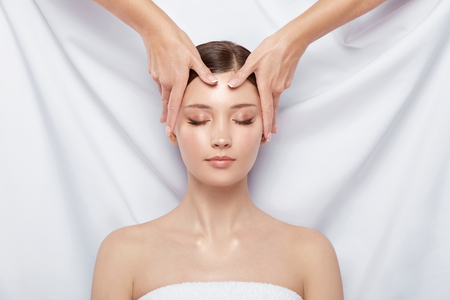girl with open shoulders having facial massage on white background, face treatment, spa procedures, woman receiving relaxationの写真素材