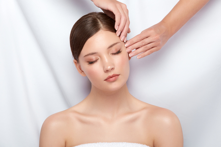 arms doing massage for beautiful woman with her eyes closed, pretty girl receiving facial treatment, skincare for attractive femaleの写真素材