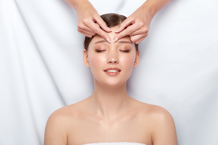 woman receiving massage for her forehead with smile on face, beautician doing facil massaging, happy customer of spaの写真素材