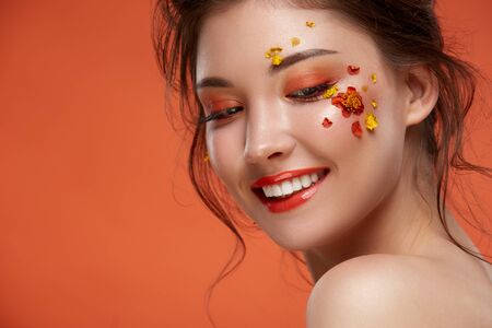 attractive girl with stylish orange make-up smiling and looking down to the side on orange...