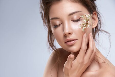pretty woman holding flower near her face with her eyes closed isolated on grey, copy space, sensual girl with white flowersの写真素材
