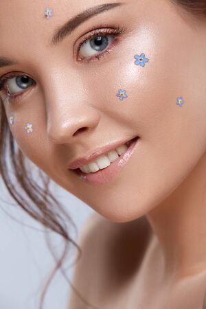 close-up of smily woman face with forget-me-nots, nude make-up with fresh flowers on young pretty ladyの写真素材