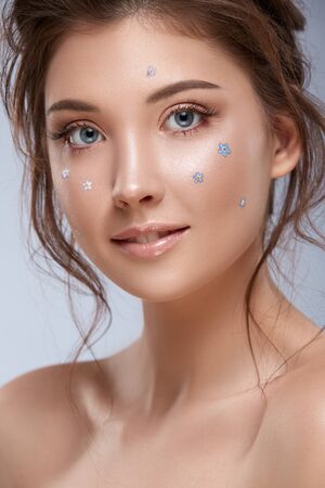 portrait of beautiful girl with fresh blue flowers on her face, pretty woman with natural make-up and nice small forget-me-notsの写真素材