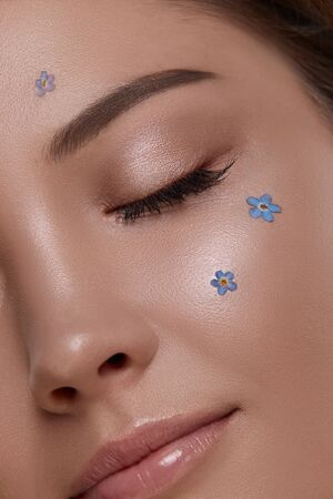close-up of womans eye with shiny make-up and fresh small flowers, closed eyes with nice mua and forget-me-notの写真素材