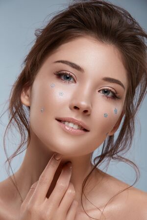 girl with fancy hairstyle and flowered make-up looking to the camera, pretty woman with curly hair and tiny flowers on faceの写真素材