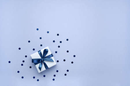 Gift box with ribbon and bow on blue background with stars shaped confetti. Top view and space for text.の写真素材