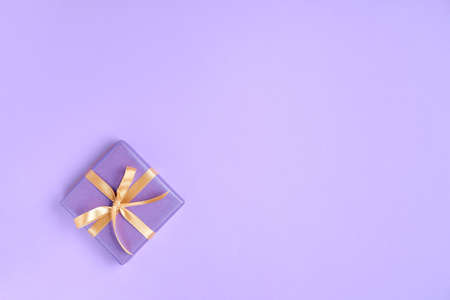 Purple gift box with golden ribbon and bow on color background. top view, copy spaceの写真素材