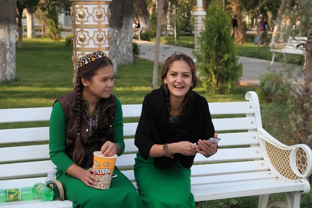 Ashgabad, Turkmenistan - October 10, 2014. Two young girls in national dress sitting on banch in park.のeditorial素材