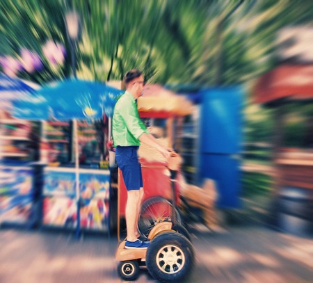 Abstract background. A young man riding a Segway in the park.  Blur effect defocusing filter applied, with vintage instagram look.の写真素材