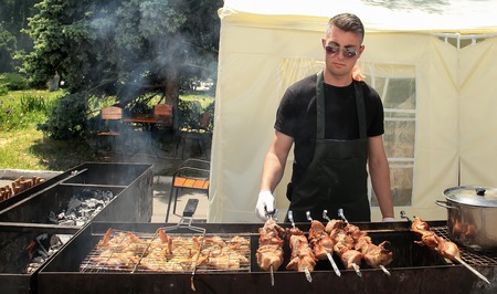 Moldova, Chisinau - 23.05.2015. BBQ fest. Young man fry a shish kebab and chicken barbecue outdoorsのeditorial素材