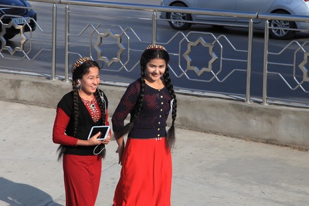 Ashgabat, Turkmenistan - October 5, 2015. Unidentified two girls in national dress and tablet in hand, walking down the main street of Ashgabat. Ashgabat, Turkmenistan - October 5, 2015.のeditorial素材