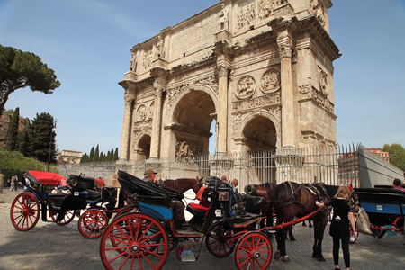 ROMA, ITALY, APRIL 7, 2016 : Coachman sits on a carriage, pulled by a horse, waiting for tourists. Arco de Constantino (Arch of Constantine) and Colosseum. The arch was erected by the Roman Senate to commemorate Constantine victory over Maxentiusの写真素材