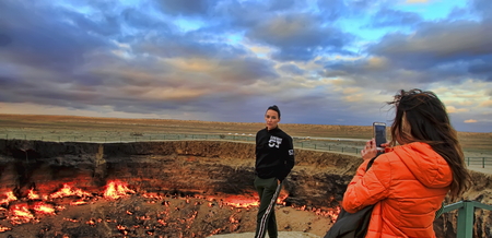 Turkmenistan, Darvaza - March 21, 2019: Girls make a photo on the background of the burning crater "Gates of Hell", Karakum desert. Darvaza is one of the ten most unusual places in the world.のeditorial素材
