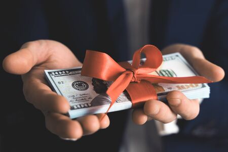 Concept, money as a gift, win or bonus. businessman takes or gives pile of 100 dollar bills tied with red ribbon with bow.の写真素材