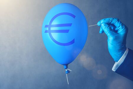Euro currency symbol on blue balloon in coronavirus time. Man hold needle directed to air balloon. Concept of finance risk.の写真素材